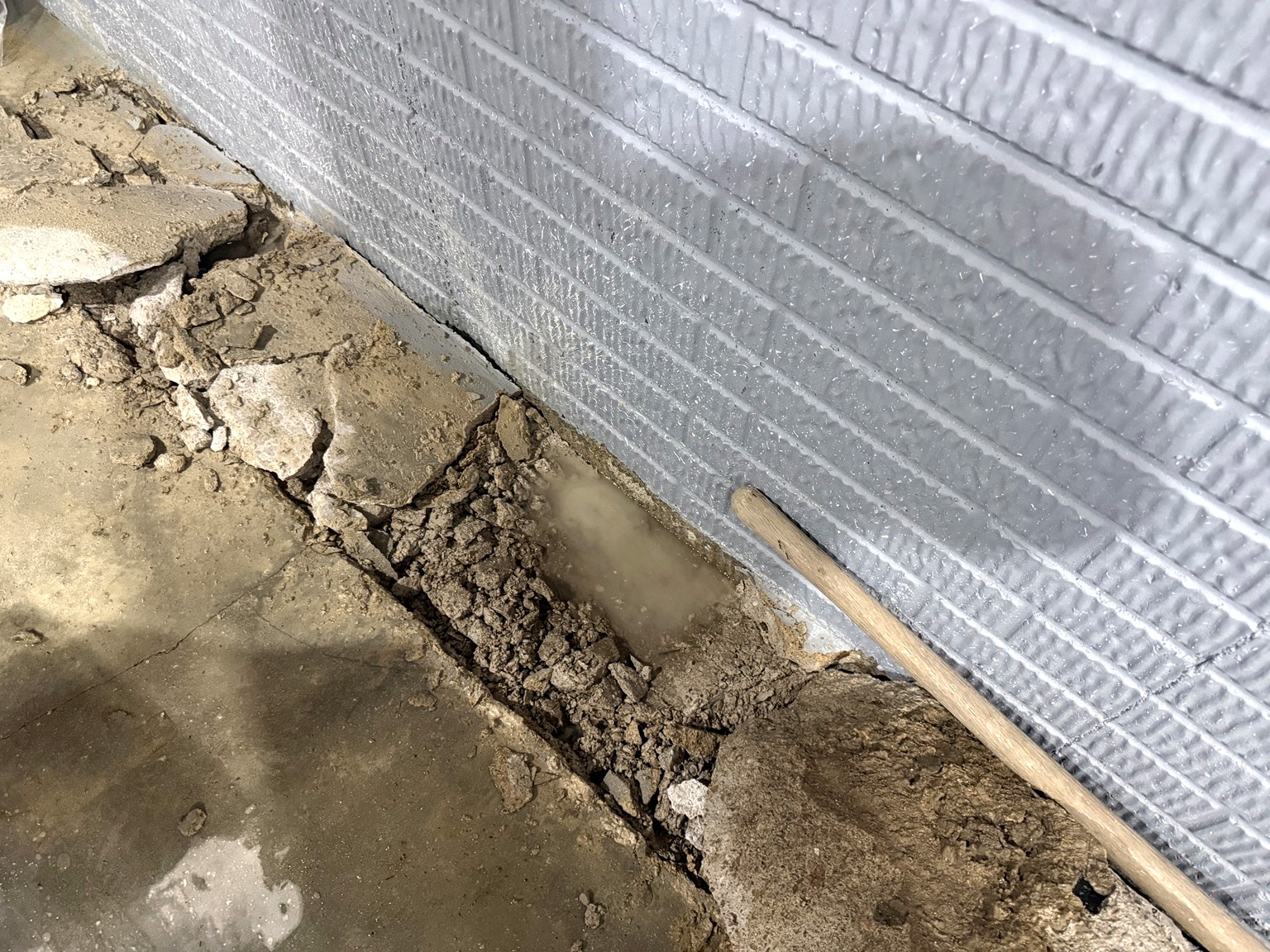Close-up of concrete floor trench beside a waterproofed basement wall